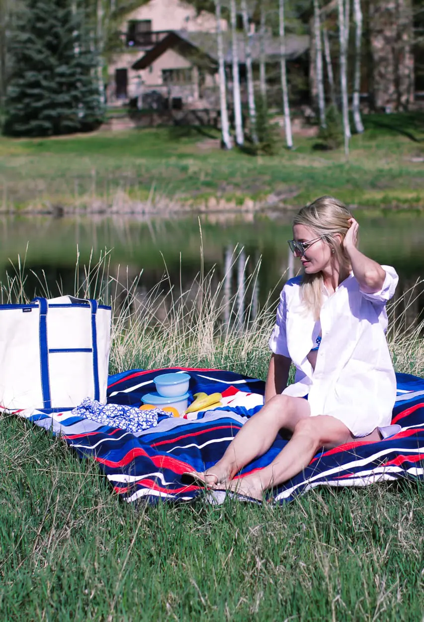stylish swim shirts and skirts on blonde woman at lake in the mountains wearing a bright blue swim skirt, white button down crinkled cotton swim cover up and a canvas blue and white tote