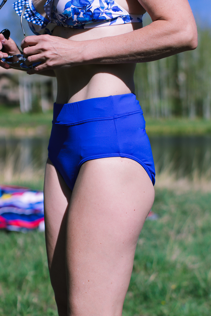 stylish swim shirts and skirts on blonde woman at lake in the mountains wearing a bright blue high waist bikini bottom