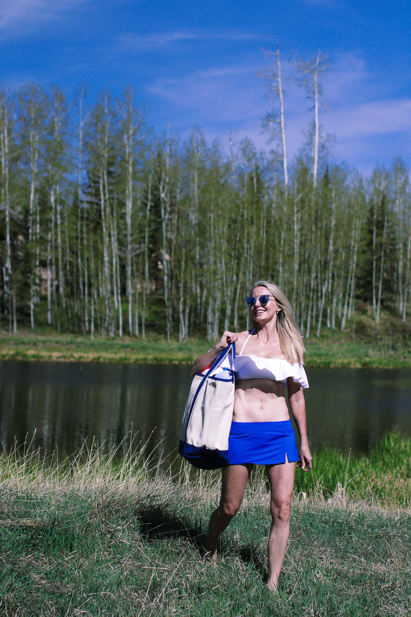 stylish swim shirts and skirts on blonde woman at lake in the mountains wearing a white bandeau ruffle bikini top and bright blue swim skirt from Lands' End