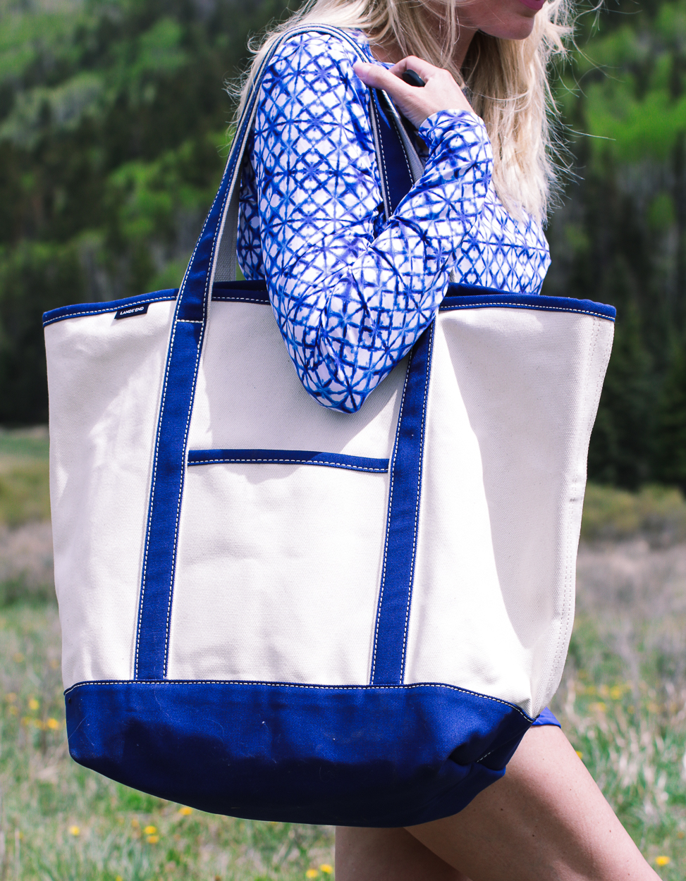 stylish swim shirts and skirts on blonde woman at lake in the mountains wearing a bright blue swim skirt, white button down crinkled cotton swim cover up and a canvas blue and white tote