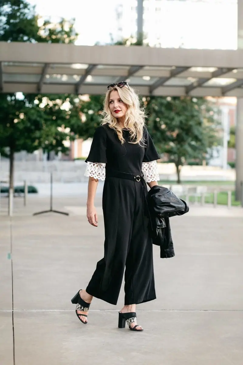 Asks black jumpsuit with wide leg over a crochet white top with black sunglasses and a black leather moto jacket