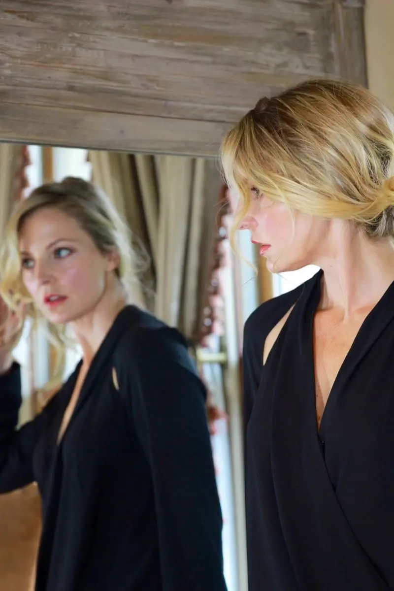 hair pulled back in a pony tail wearing a black blouse with shoulder sliver cutouts