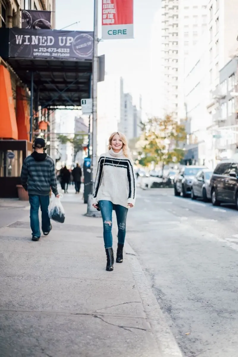 erin busbee walking down new york city street wearing casual outfit including dark wash citizens of humanity rocket slightly distressed skinny jeans, mid-calf black booties by sam edelman, and a pam and gela racing stripe turtleneck sweater