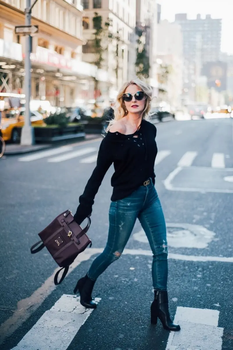 erin busbee from busbeestyle.com crossing nyc street in black laceup sweater with distressed skinny jeans by citizens of humanity rocket jeans, black booties, and henri bendel jetsetter backpack