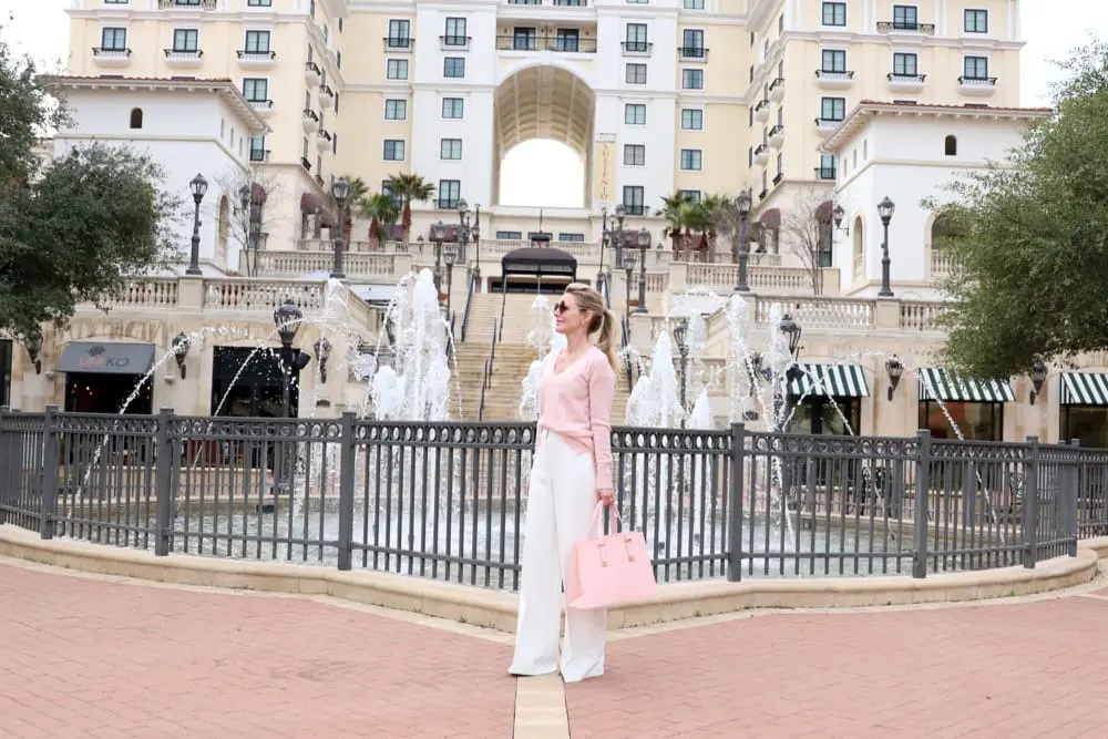 Beautiful wide leg, high rise winter white pants by milly from nordstrom paired with a pale or light pink, v-neck cashmere sweater and a gorgeous over-sized trapeze shaped pink top handle satchel handbag by ted baker