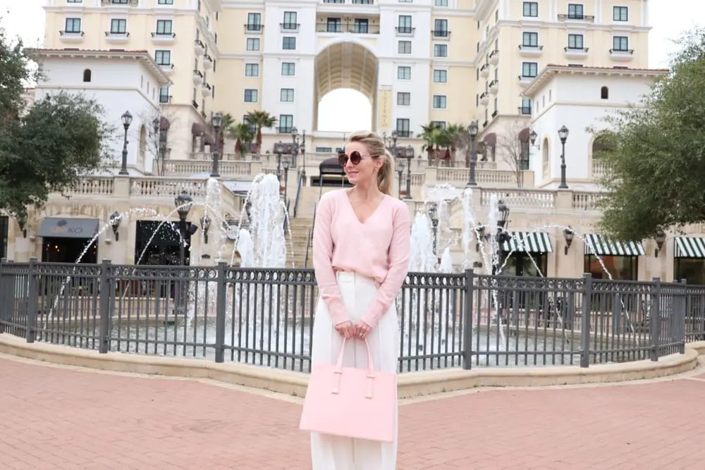 Beautiful wide leg, high rise winter white pants by milly from nordstrom paired with a pale or light pink, v-neck cashmere sweater and a gorgeous over-sized trapeze shaped pink top handle satchel handbag by ted baker