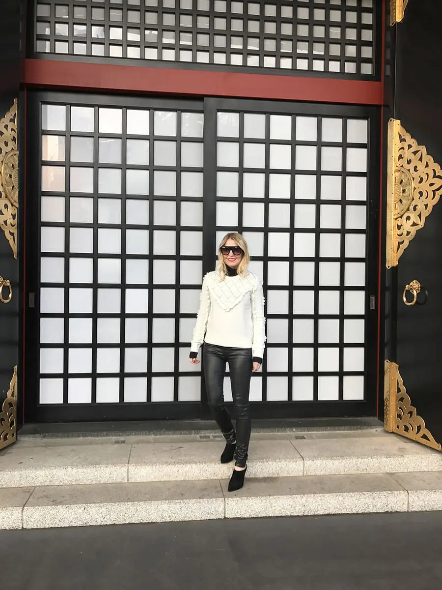 Erin busbee wearing a white topshop sweater with pom pom detailing, faux leather black skinny jeans by citizens of humanity called the "rocket" jeans, mules by marc fisher in black suede and flat top sunglasses that look like Givenchy but only cost $10 from Amazon fashion