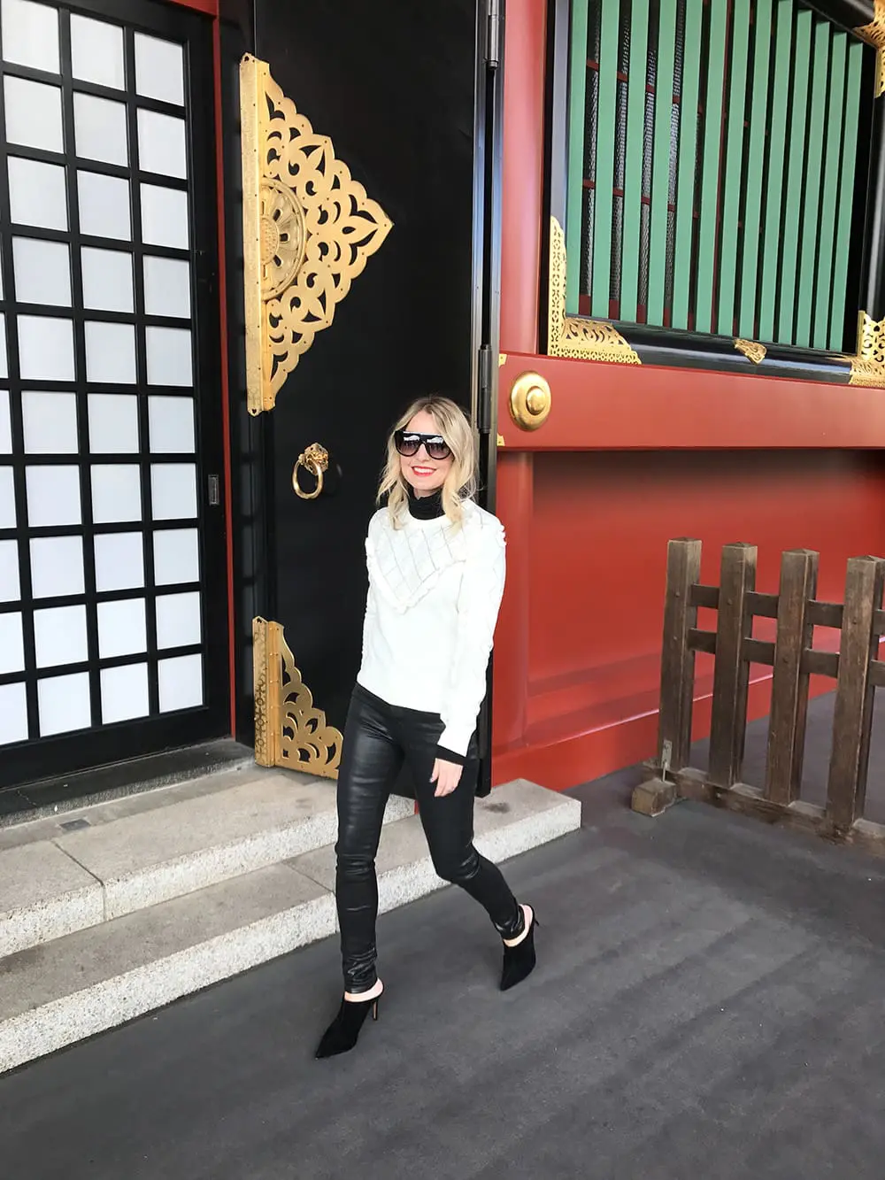 Erin busbee wearing a white topshop sweater with pom pom detailing, faux leather black skinny jeans by citizens of humanity called the "rocket" jeans, mules by marc fisher in black suede and flat top sunglasses that look like Givenchy but only cost $10 from Amazon fashion