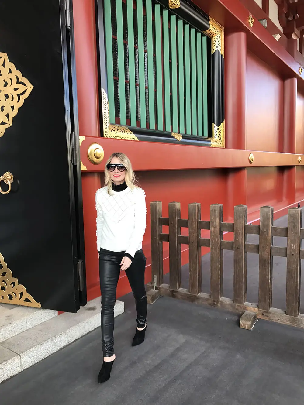 Erin busbee wearing a white topshop sweater with pom pom detailing, faux leather black skinny jeans by citizens of humanity called the "rocket" jeans, mules by marc fisher in black suede and flat top sunglasses that look like Givenchy but only cost $10 from Amazon fashion