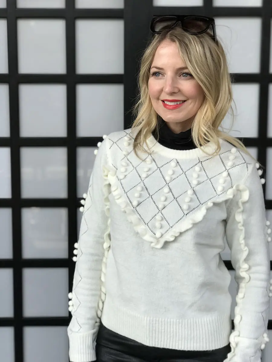 Erin busbee wearing a white topshop sweater with pom pom detailing, faux leather black skinny jeans by citizens of humanity called the "rocket" jeans, mules by marc fisher in black suede and flat top sunglasses that look like Givenchy but only cost $10 from Amazon fashion