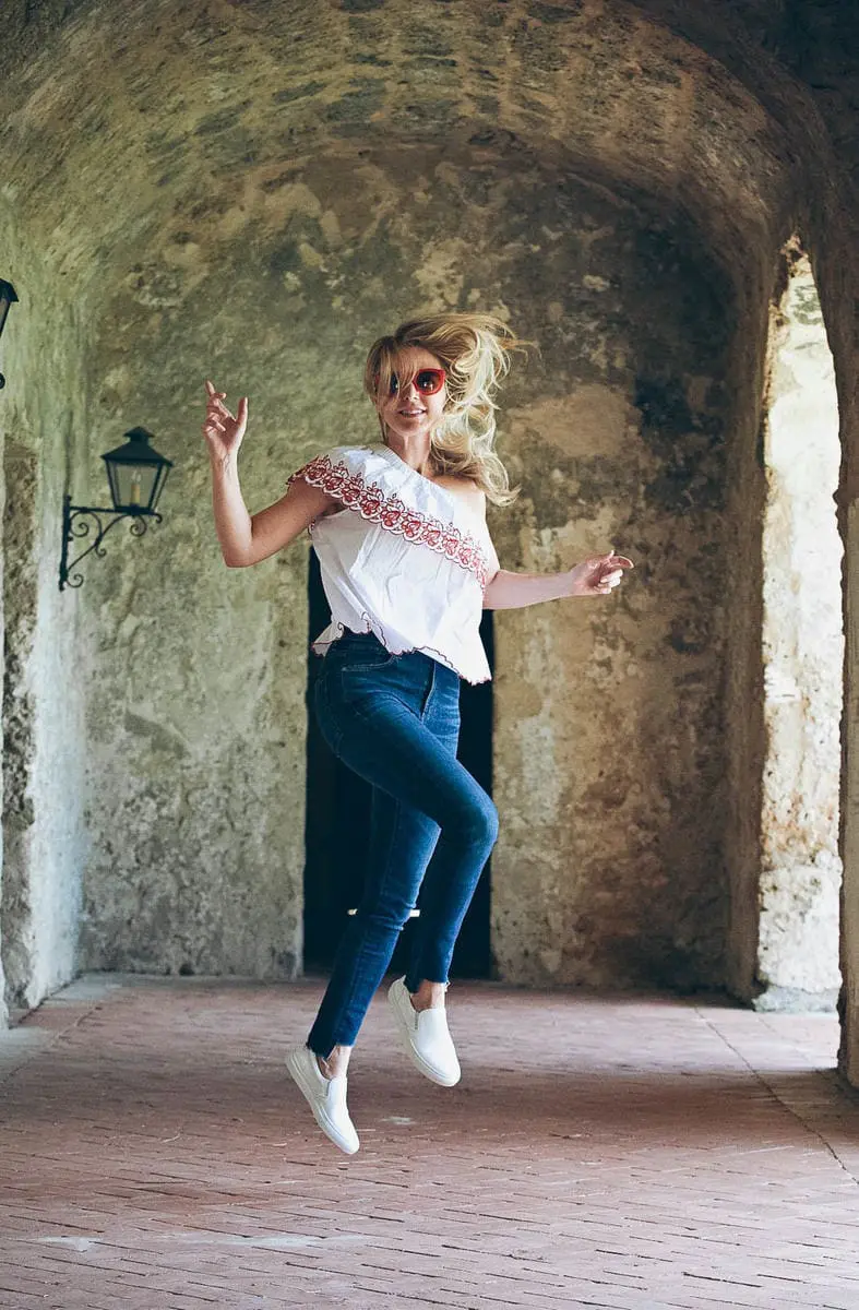 White sneakers, slip on sneakers called the Wooster, by Greats brand, worn 2 ways, including an ivory trench coat, and eyelet top with dark wash skinny jeans, and a one shoulder red and white top with red sunglasses, on Erin Busbee fashion blogger and youtuber of BusbeeStyle
