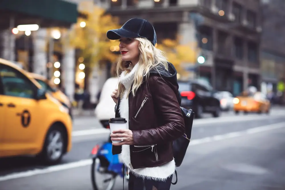 Gym to street pants, perfect for creating the athleisure look on fashion blogger over 40, Erin Busbee of Busbee Style paired with fuzzy white turtleneck sweater, doma leather hooded leather jacket and Henri Bendel leather jetsetter backpack with patent leather sneakers by Kenneth Cole