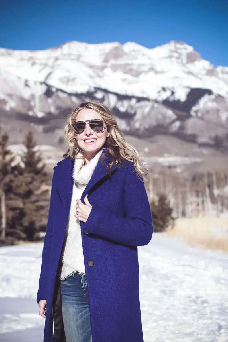 blue coat by Elie Tahari, boiled wool winter coat in beautiful color on fashion blogger over 40, Erin Busbee of Busbee Style wearing Henri Bendel sunglasses, Sorel conquest wedge booties, Amo twist skinny jeans and a Bloomingdales fuzzy white sweater in mountain village, colorado, snowy mountains