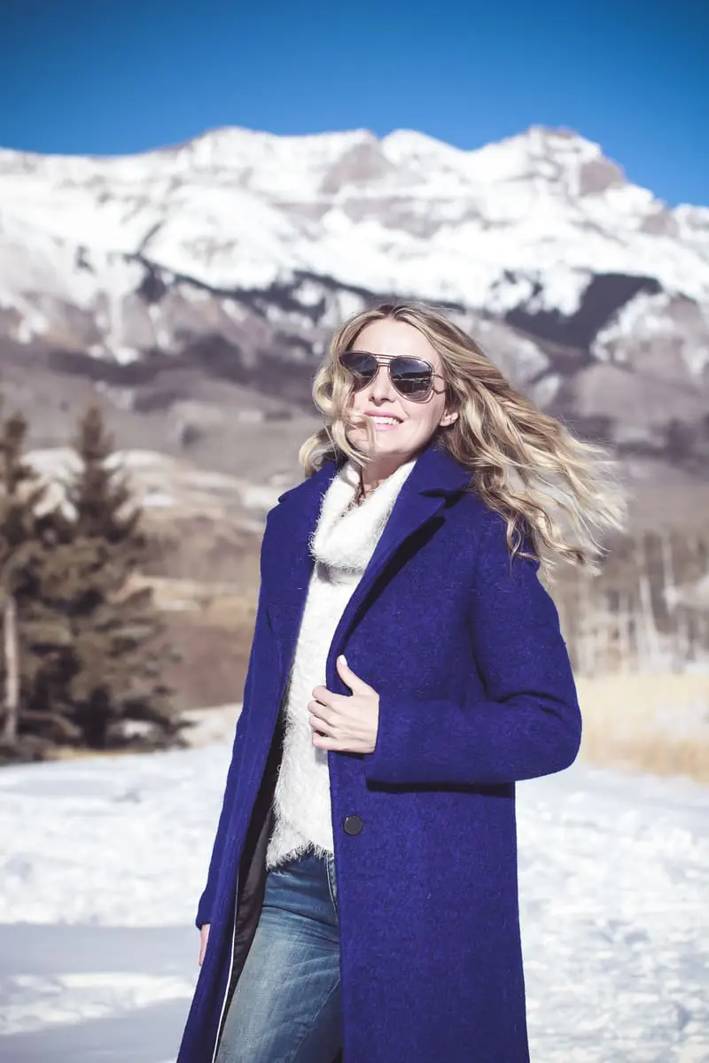blue coat by Elie Tahari, boiled wool winter coat in beautiful color on fashion blogger over 40, Erin Busbee of Busbee Style wearing Henri Bendel sunglasses, Sorel conquest wedge booties, Amo twist skinny jeans and a Bloomingdales fuzzy white sweater in mountain village, colorado, snowy mountains