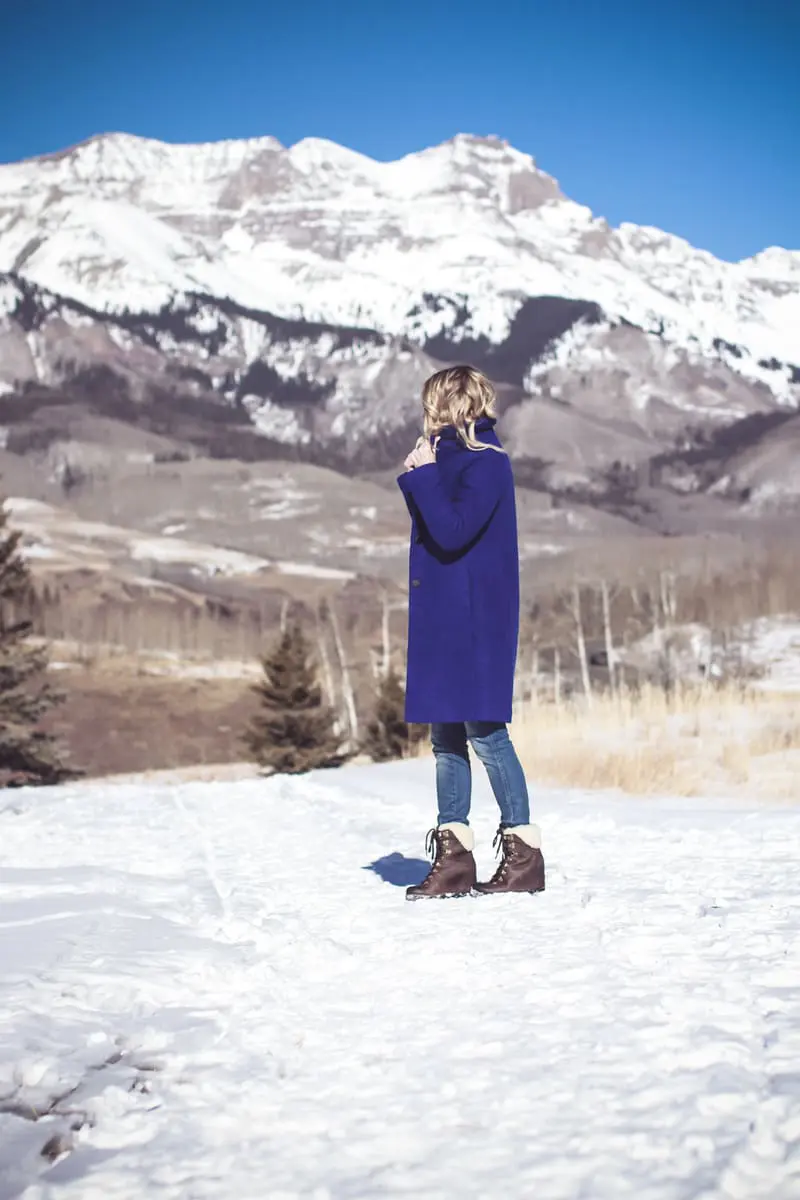 blue coat by Elie Tahari, boiled wool winter coat in beautiful color on fashion blogger over 40, Erin Busbee of Busbee Style wearing Henri Bendel sunglasses, Sorel conquest wedge booties, Amo twist skinny jeans and a Bloomingdales fuzzy white sweater in mountain village, colorado, snowy mountains