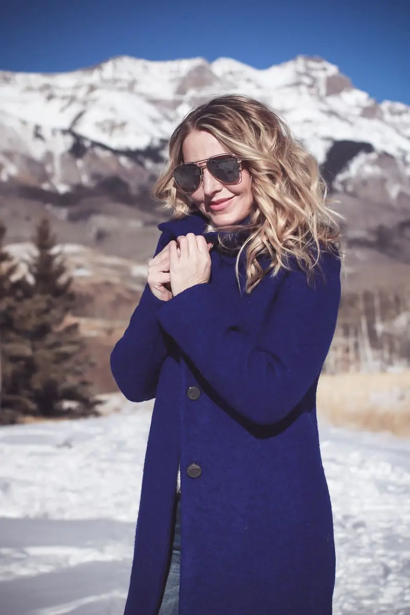 blue coat by Elie Tahari, boiled wool winter coat in beautiful color on fashion blogger over 40, Erin Busbee of Busbee Style wearing Henri Bendel sunglasses, Sorel conquest wedge booties, Amo twist skinny jeans and a Bloomingdales fuzzy white sweater in mountain village, colorado, snowy mountains