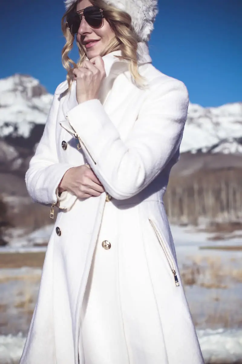 White coat, winter white coat, double breasted by Guess in boucle, paired with Sorel Conquest booties, Amo twist skinny jeans, a white fuzzy hat and a fuzzy white sweater, on Fashion Blogger over 40, Erin Busbee of Busbee Style, BusbeeStyle.com