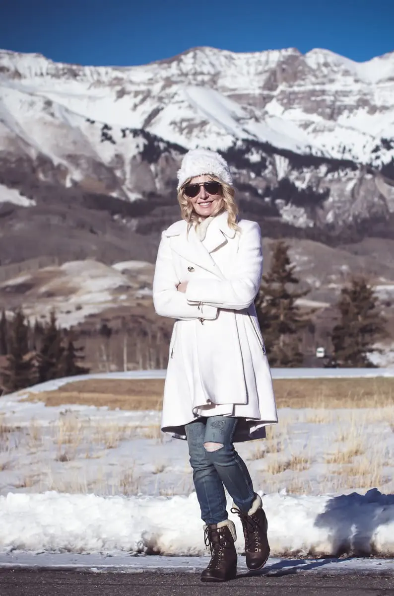 White coat, winter white coat, double breasted by Guess in boucle, paired with Sorel Conquest booties, Amo twist skinny jeans, a white fuzzy hat and a fuzzy white sweater, on Fashion Blogger over 40, Erin Busbee of Busbee Style, BusbeeStyle.com in telluride, Colorado in the snowy mountains