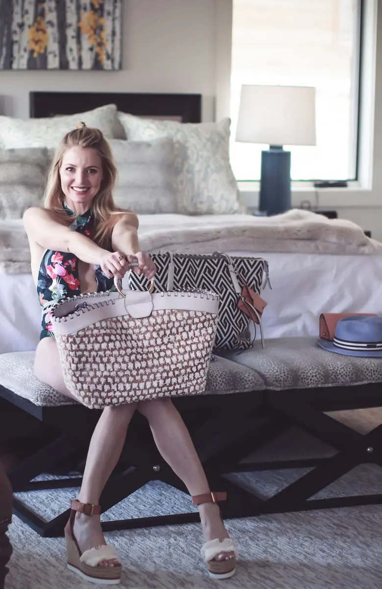 Best accessories featuring a beautiful beach bag in beige and white with circle handle from Henri Bendel on fashion blogger over 40, Erin Busbee of Busbee Style wearing a La Blanca tropical print one piece swimsuit