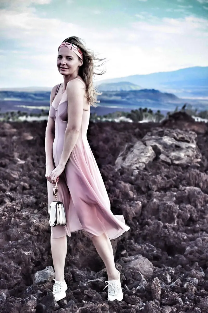 blond woman standing on lava rock in Hawaii wearing a blush corset sheer swim dress by Norma Kamali and floral headband from Nordstrom
