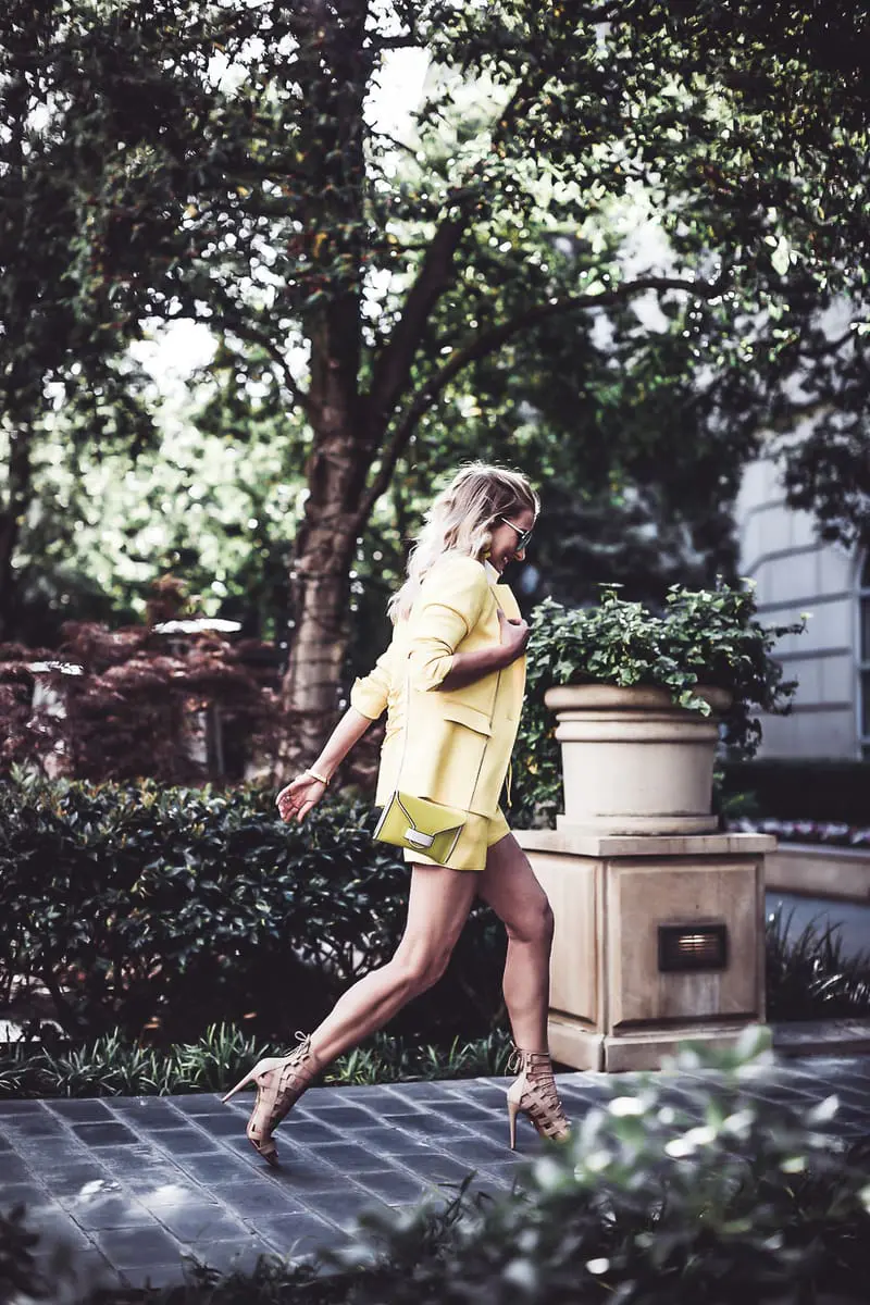 reward style blogger conference 2018, blonde fashion blogger walking in a yellow shorts suit by Veronica Beard at Hotel Crescent court carrying a Henri Bendel Rivington pouch in bright yellow