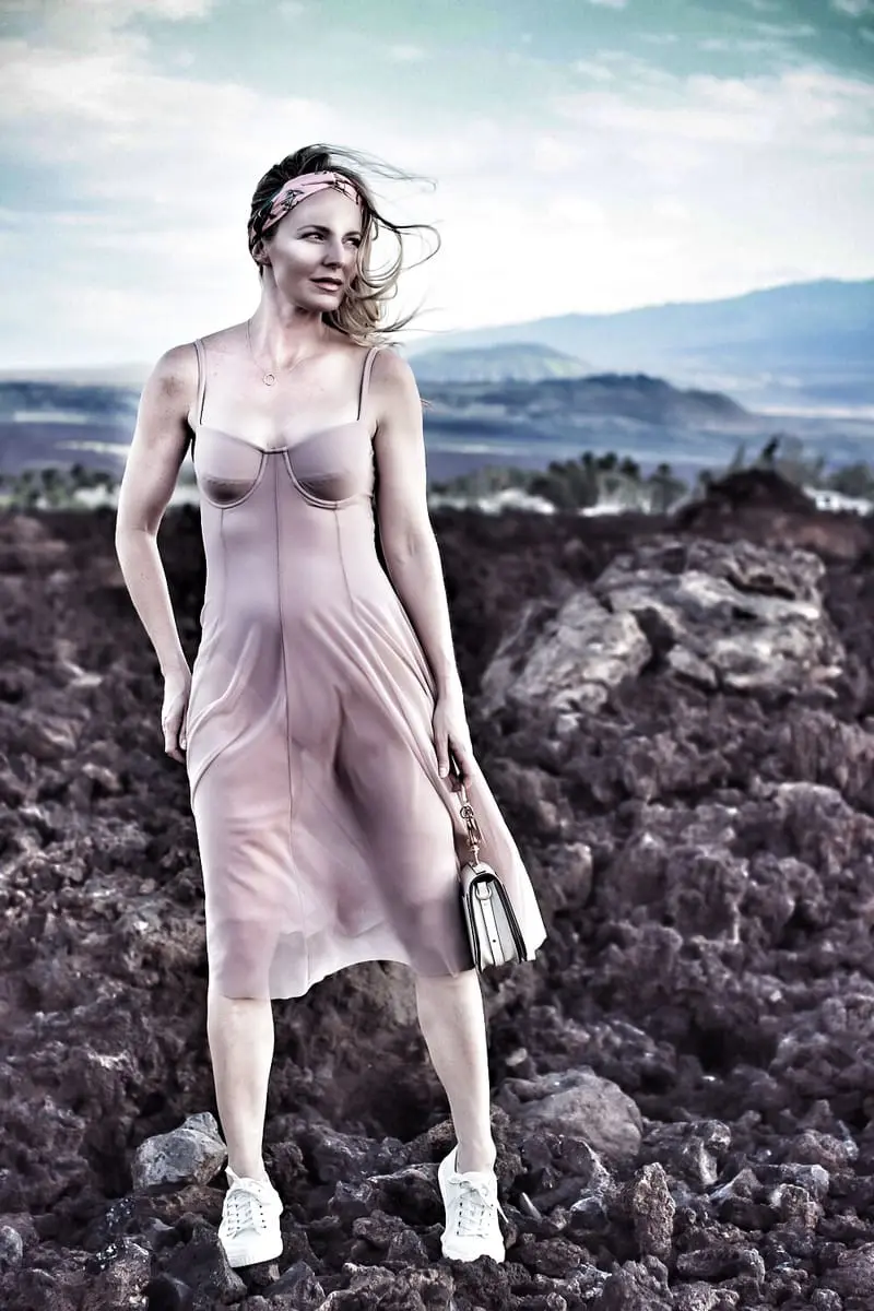 blond woman standing on lava rock in Hawaii wearing a blush corset sheer swim dress by Norma Kamali and floral headband from Nordstrom