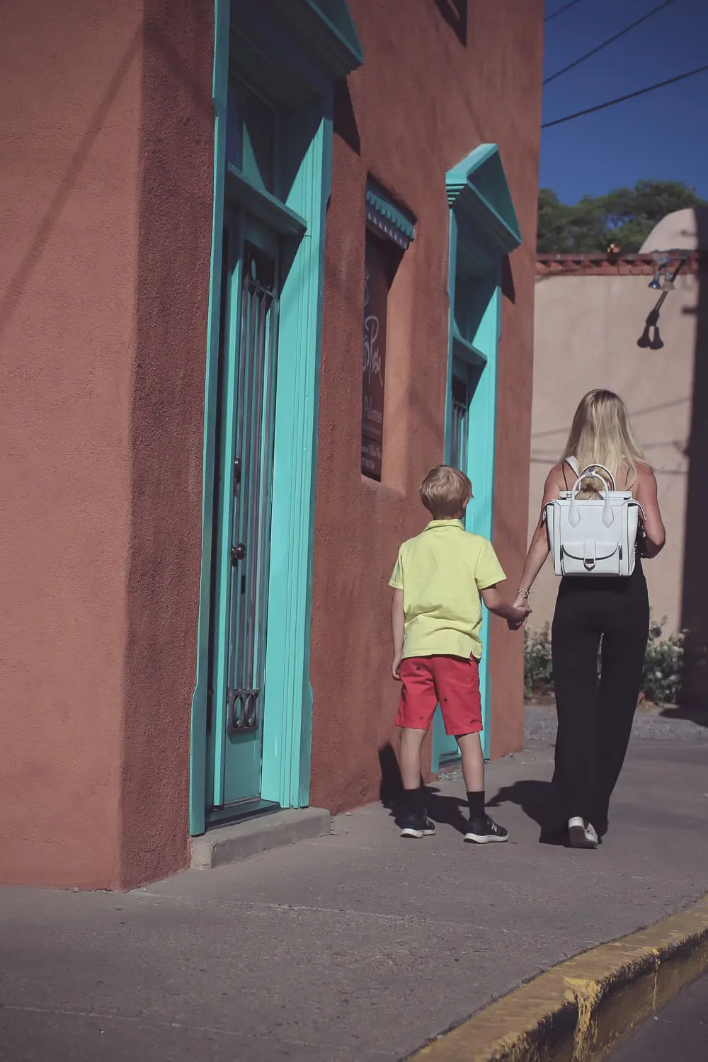 chic and sophisticated backpacks for grown ups by Henri Bendel, featuring blonde woman carrying a white Rivington convertible tote and backpack wearing all black with dainty gold and green jewelry