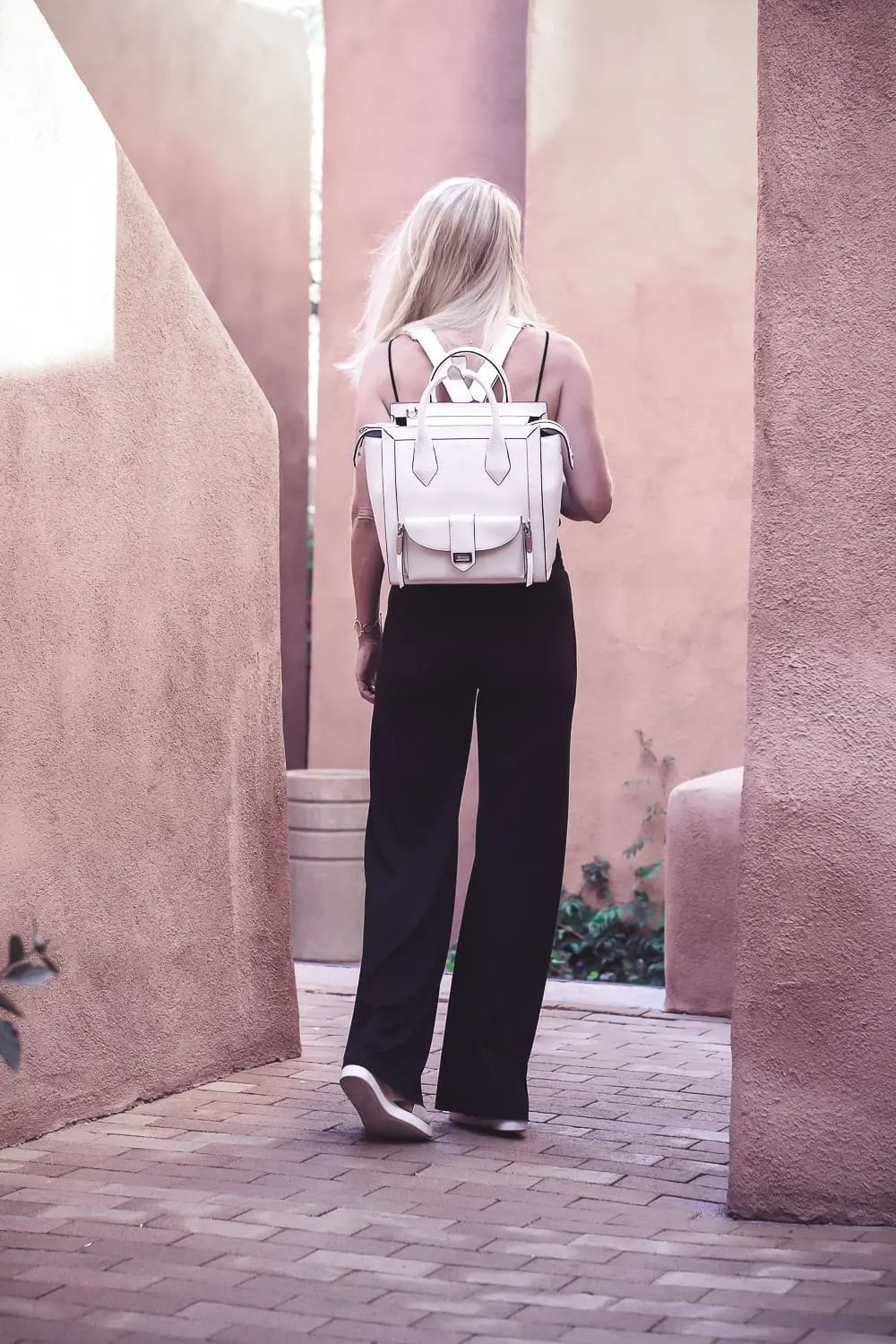 chic and sophisticated backpacks for grown ups by Henri Bendel, featuring blonde woman carrying a white Rivington convertible tote and backpack wearing all black with dainty gold and green jewelry