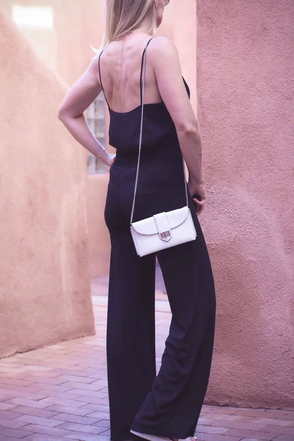 chic and sophisticated backpacks for grown ups by Henri Bendel, featuring blonde woman carrying a white Rivington convertible tote and backpack wearing all black with dainty gold and green jewelry