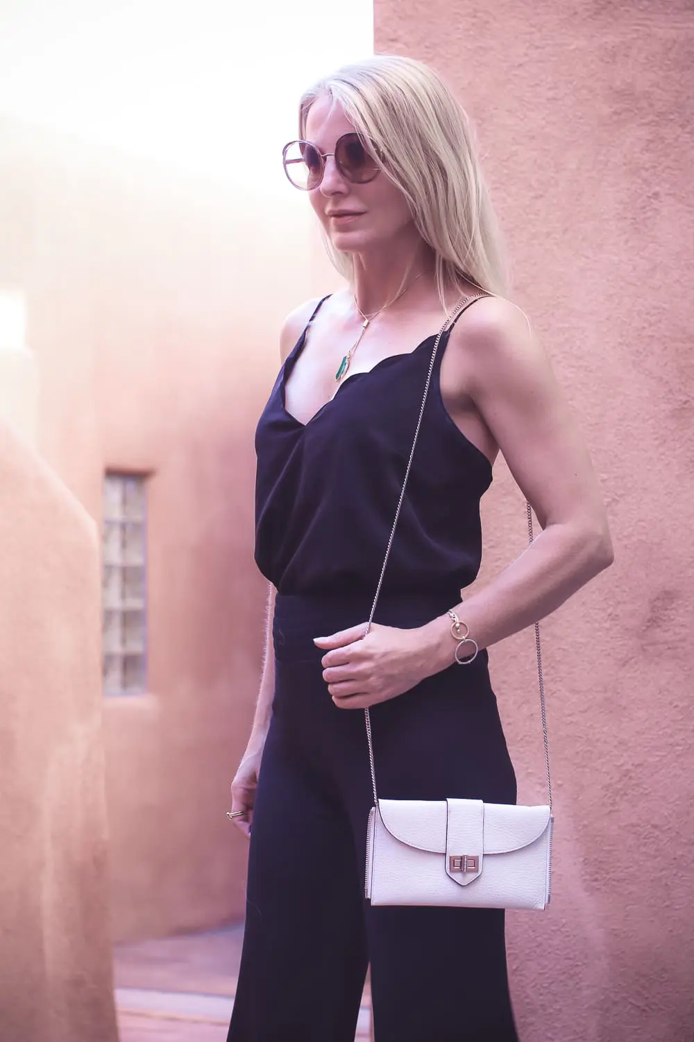 chic and sophisticated backpacks for grown ups by Henri Bendel, featuring blonde woman carrying a white Rivington convertible tote and backpack wearing all black with dainty gold and green jewelry