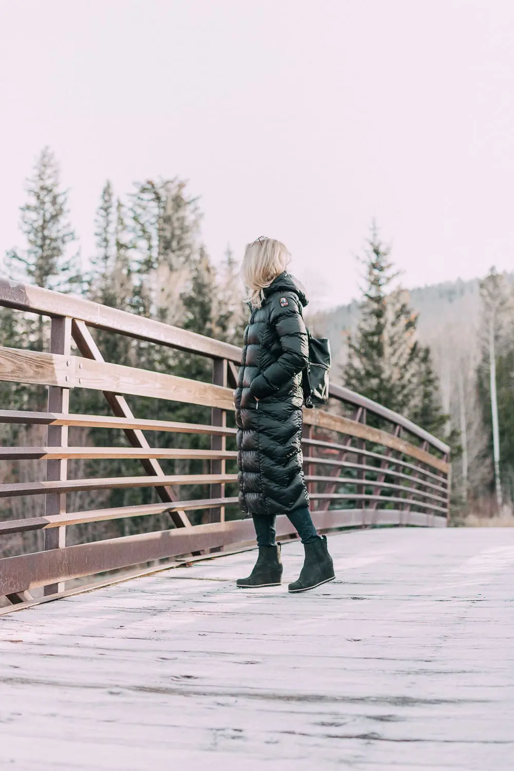 best puffer coats for women by Parajumpers from Bloomingdales in black, long puffer coat paired with dark jeans, black Ugg wedge booties on blonde woman