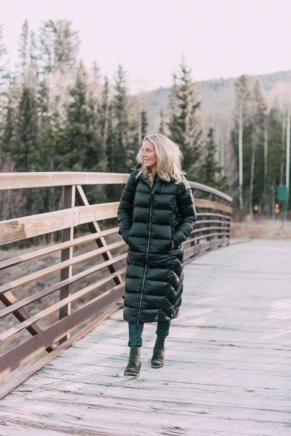 best puffer coats for women by Parajumpers from Bloomingdales in black, long puffer coat paired with dark jeans, black Ugg wedge booties on blonde woman
