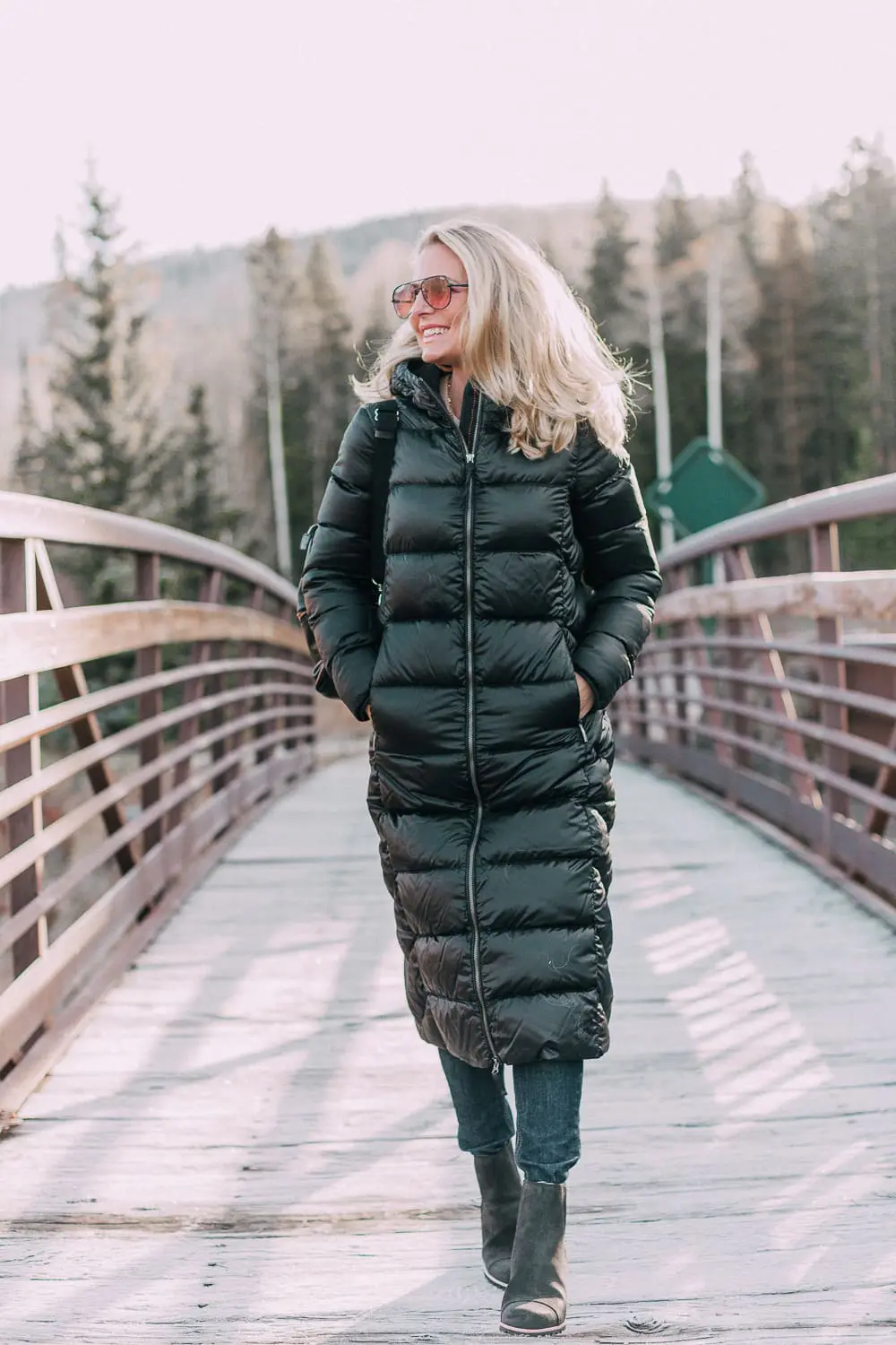 best puffer coats for women by Parajumpers from Bloomingdales in black, long puffer coat paired with dark jeans, black Ugg wedge booties on blonde woman