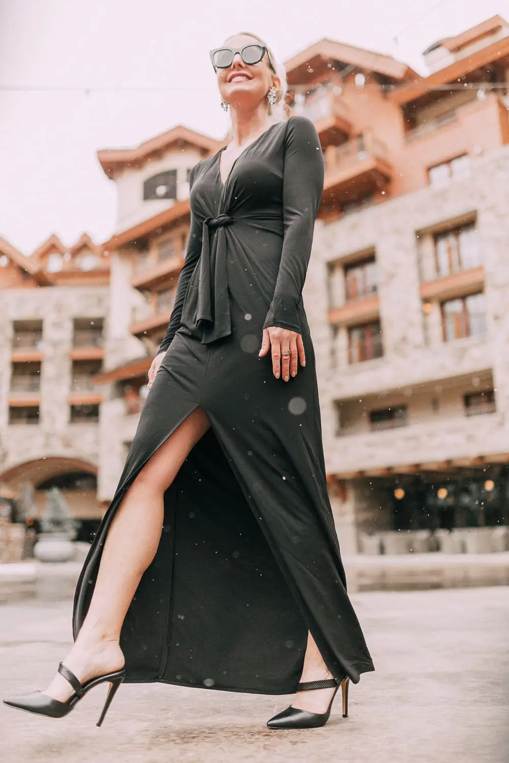 Unexpected holiday party outfits featuring a long black maxi dress with high slit to show off legs and a knot under the bust on blonde fashion blogger in telluride, colorado in the snow