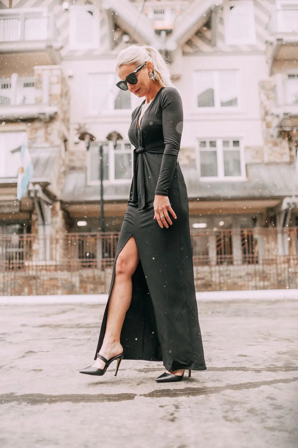 Unexpected holiday party outfits featuring a long black maxi dress with high slit to show off legs and a knot under the bust on blonde fashion blogger in telluride, colorado in the snow
