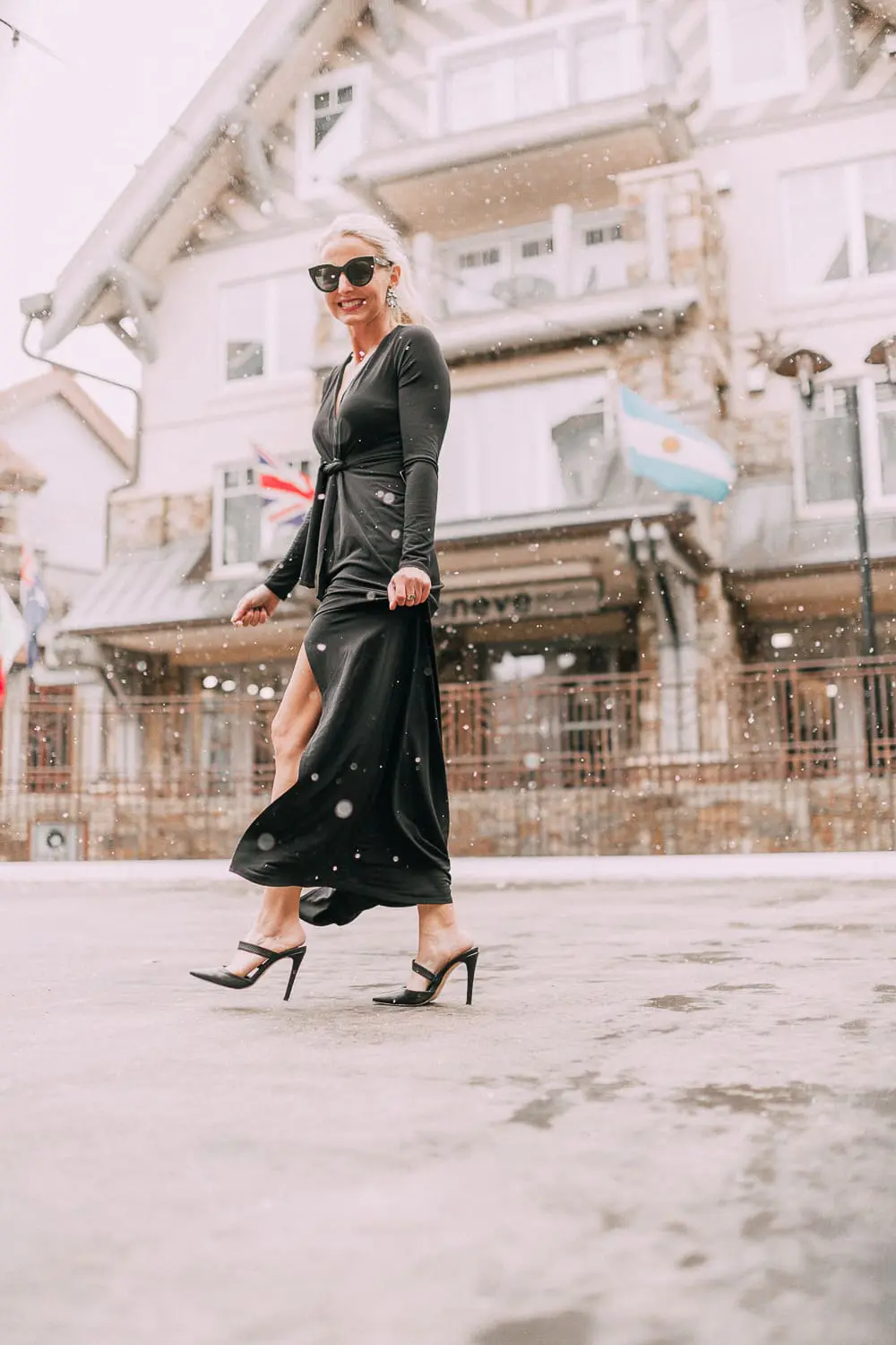 Unexpected holiday party outfits featuring a long black maxi dress with high slit to show off legs and a knot under the bust on blonde fashion blogger in telluride, colorado in the snow