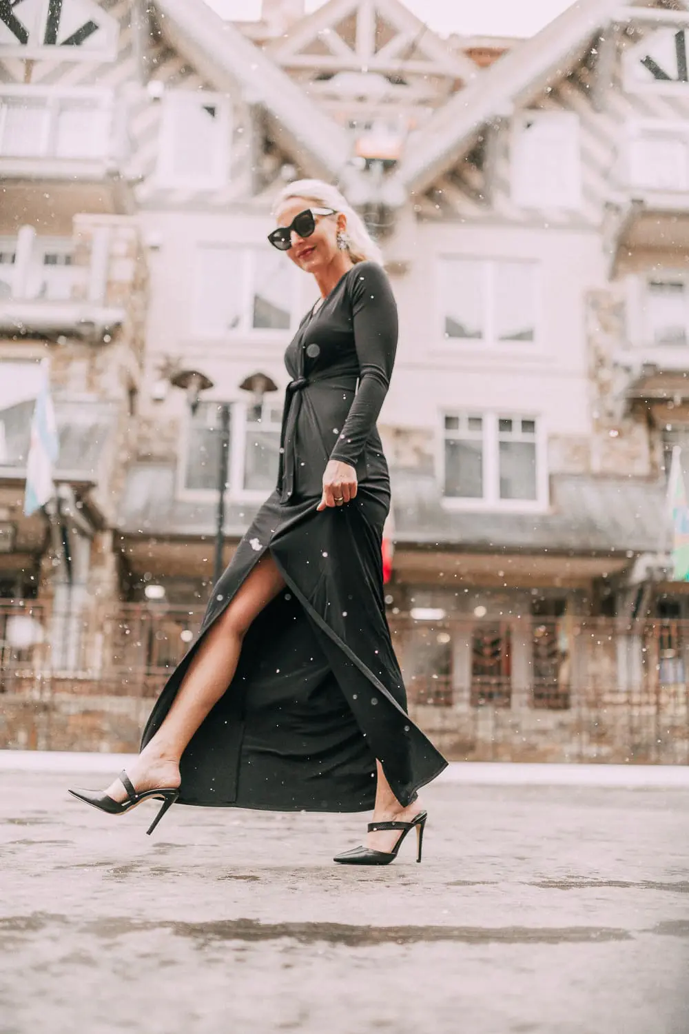 Unexpected holiday party outfits featuring a long black maxi dress with high slit to show off legs and a knot under the bust on blonde fashion blogger in telluride, colorado in the snow