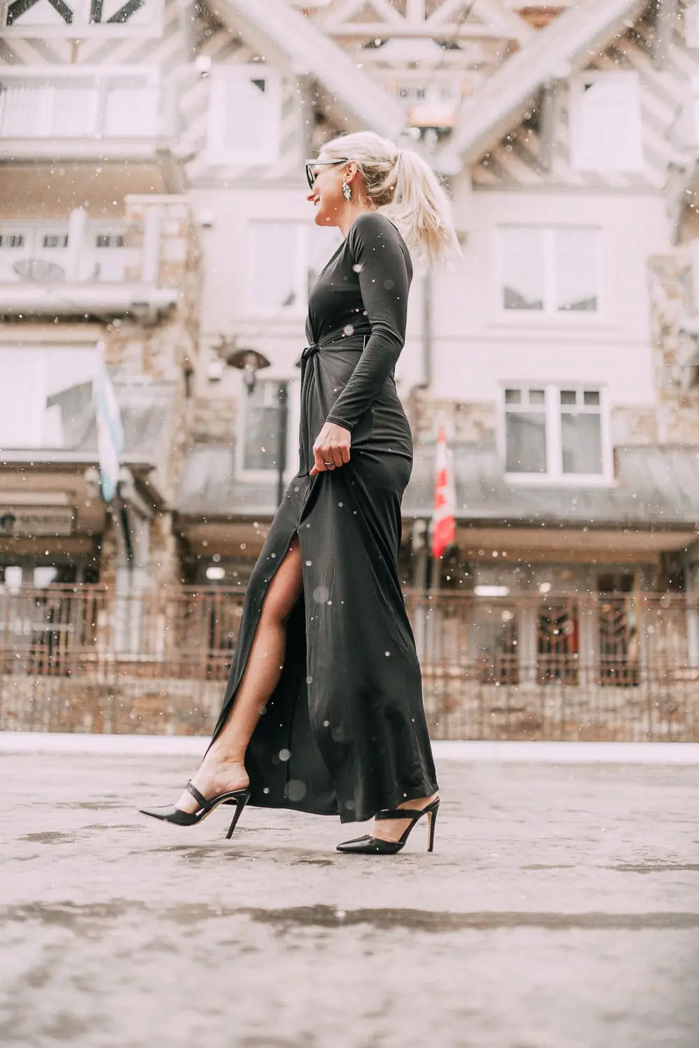 Unexpected holiday party outfits featuring a long black maxi dress with high slit to show off legs and a knot under the bust on blonde fashion blogger in telluride, colorado in the snow