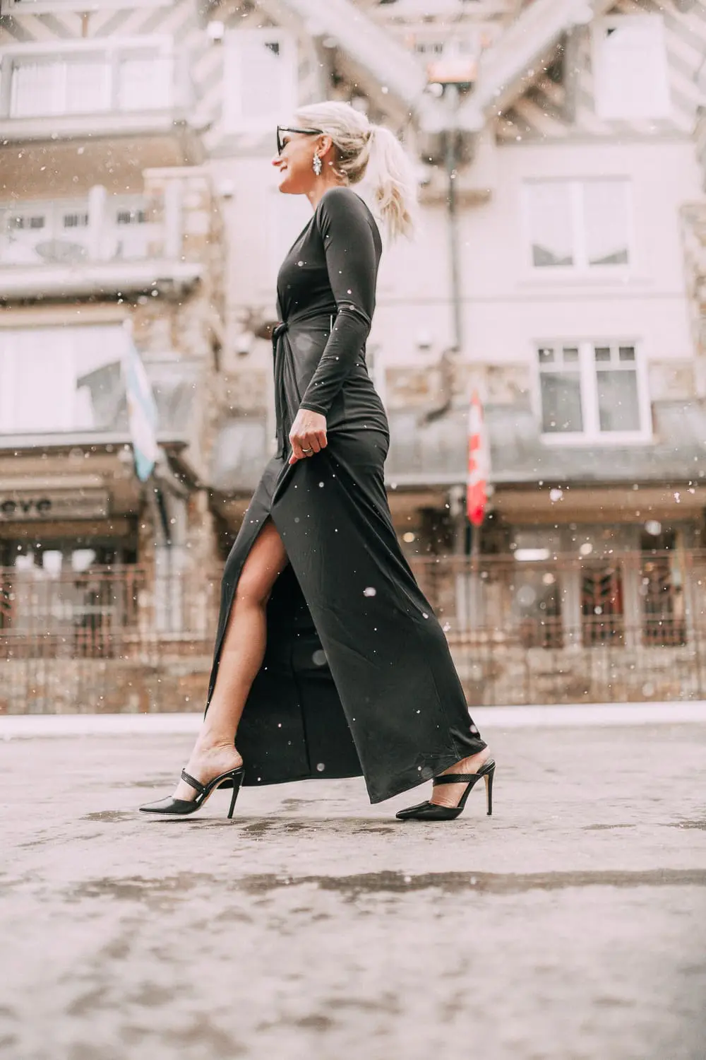 Unexpected holiday party outfits featuring a long black maxi dress with high slit to show off legs and a knot under the bust on blonde fashion blogger in telluride, colorado in the snow