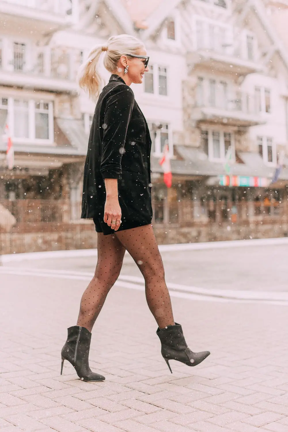 Unexpected holiday party outfits featuring a velvet Shorts suit from Express paired with Western black booties, and polka dot black tights on fashion blogger with blonde hair