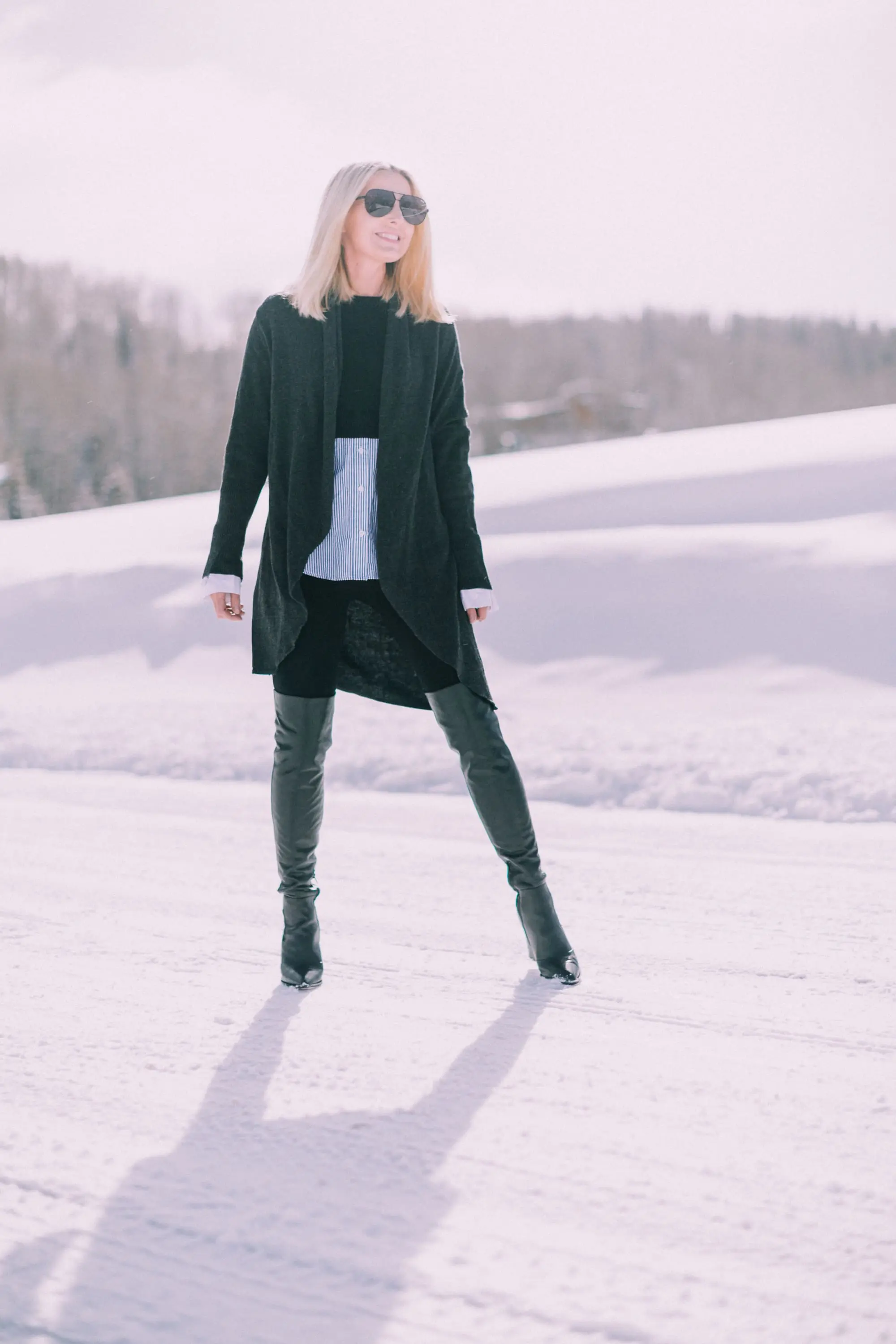 blond fashion blogger over 40 showing how to wear black Spanx leggings in an outfit with Sam Edelman Valda over the knee boots and Barefoot Dreams cardigan in the snow
