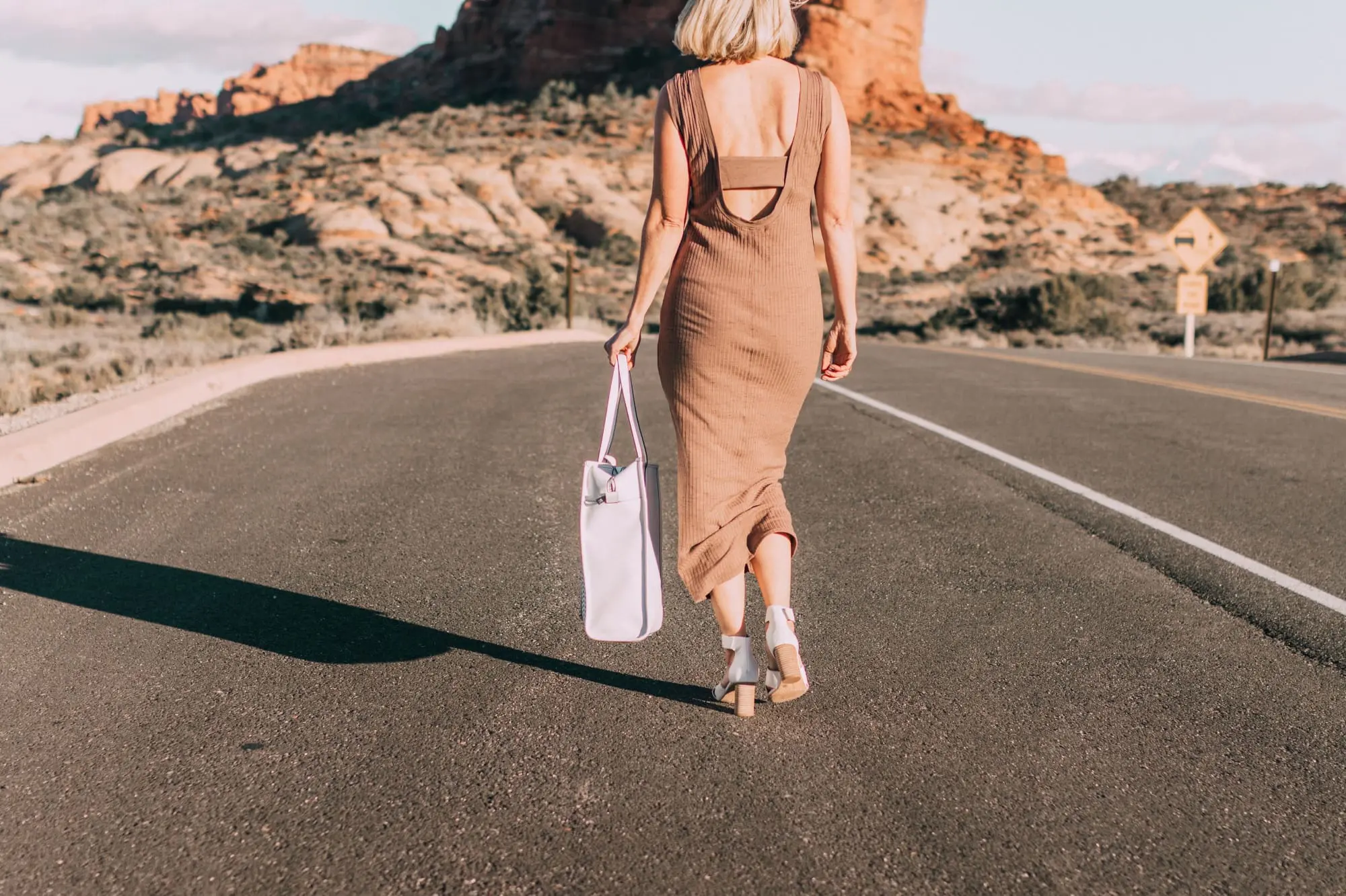 Spring Handbags, Fashion blogger Erin Busbee of BusbeeStyle.com wearing a brown sweater dress by David Lerner from Revolve, a white perforated tote bag fromVince Camuto, and white ankle strap sandals from Vince Camuto in Moab, Utah