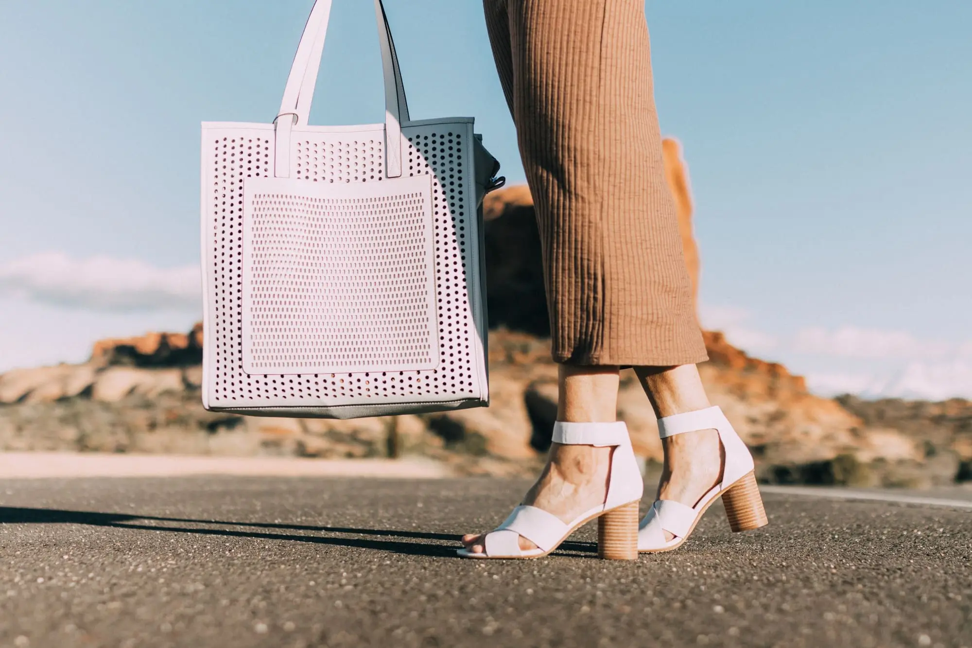Spring Handbags, Fashion blogger Erin Busbee of BusbeeStyle.com wearing a brown sweater dress by David Lerner from Revolve, a white perforated tote bag fromVince Camuto, and white ankle strap sandals from Vince Camuto in Moab, Utah