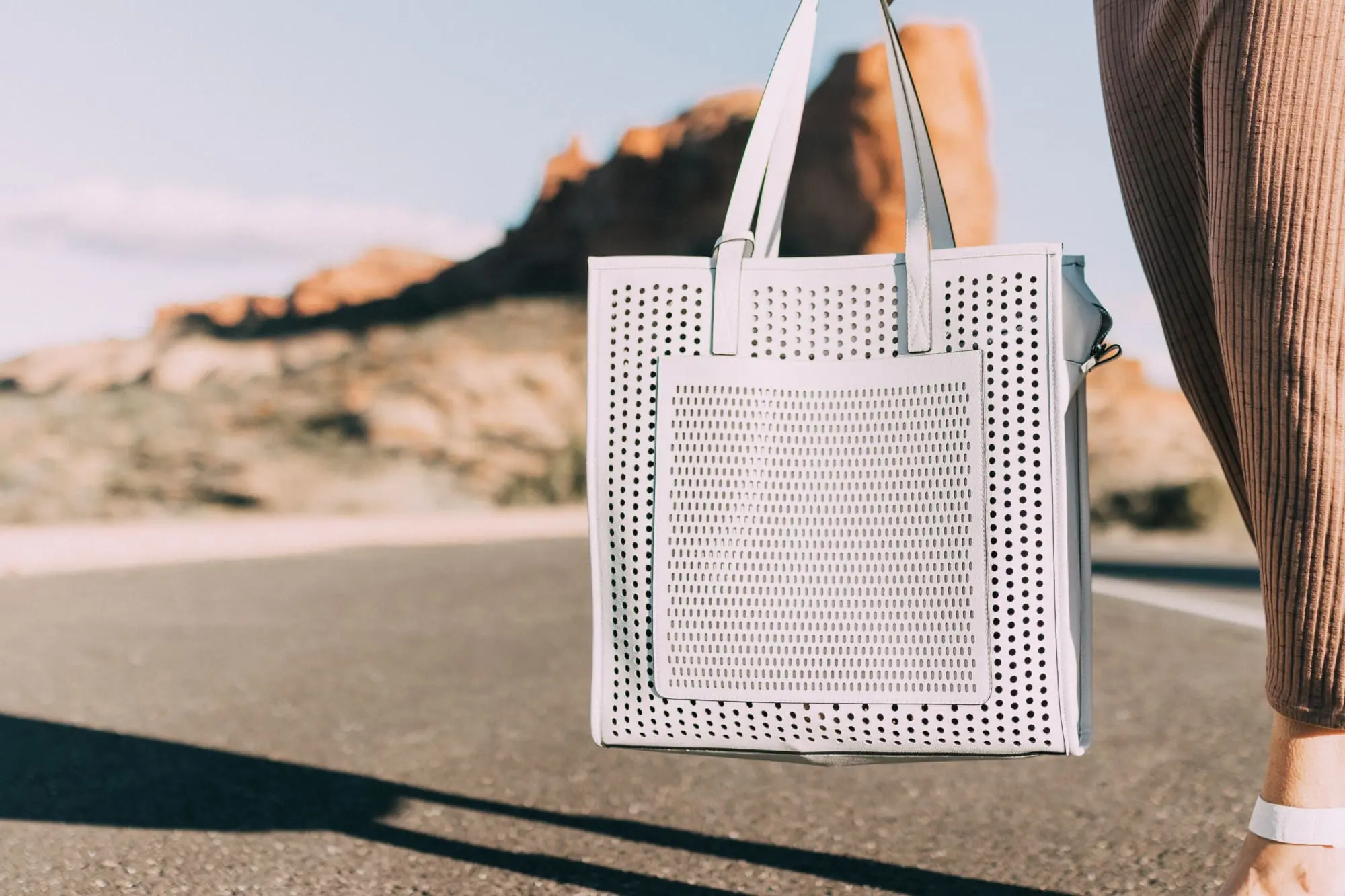 Spring Handbags, Fashion blogger Erin Busbee of BusbeeStyle.com wearing a brown sweater dress by David Lerner from Revolve, a white perforated tote bag fromVince Camuto, and white ankle strap sandals from Vince Camuto in Moab, Utah