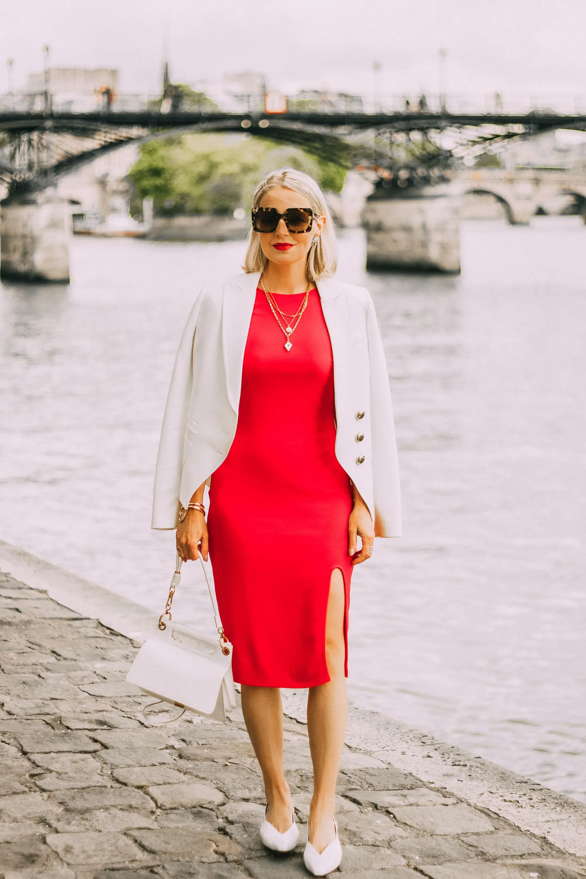 erin busbee wearing red quarter sleeve midi length sheath dress with slit ivory smythe wrap blazer draped over shoulders paired with white slingback heeled mules 