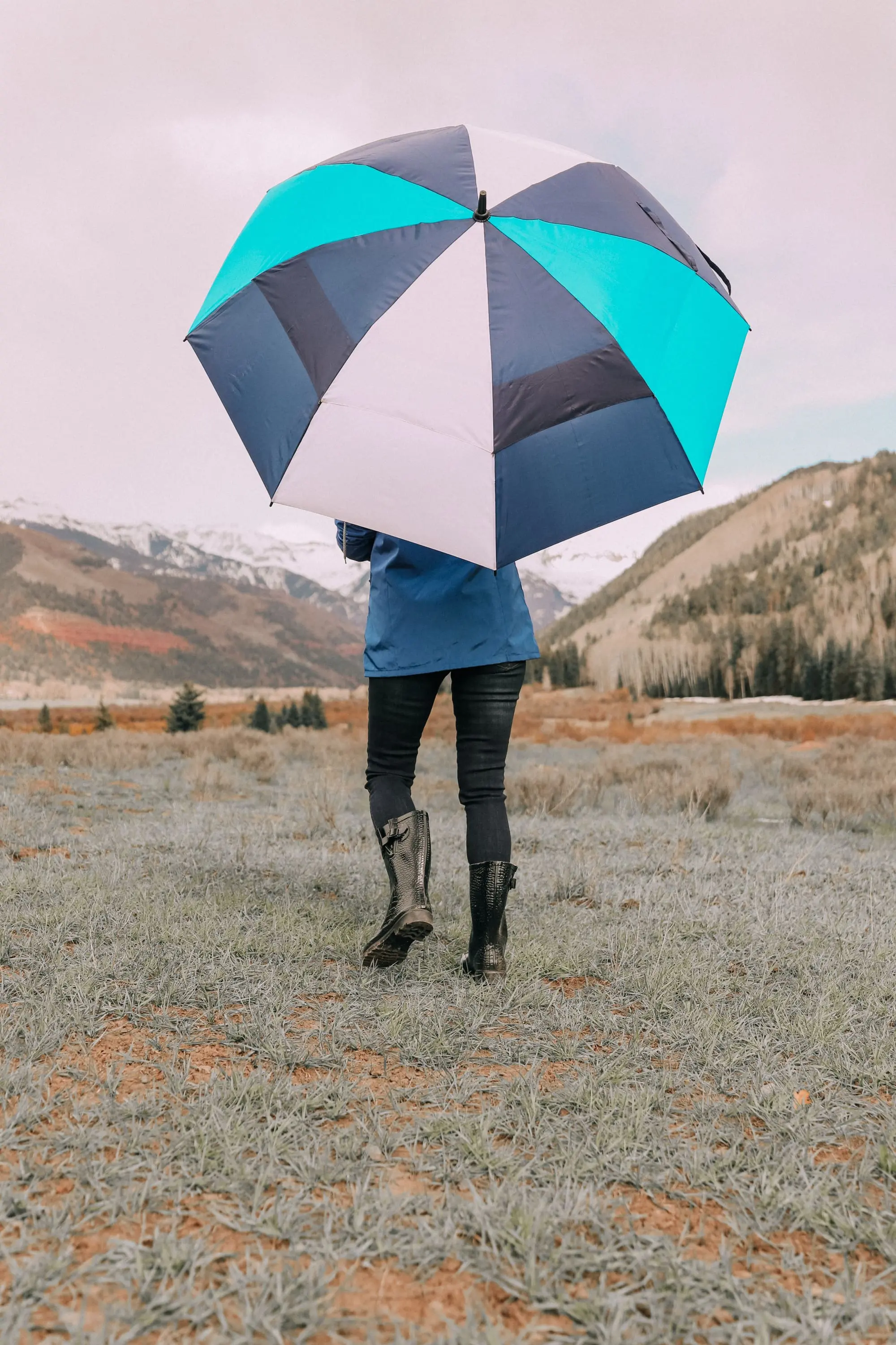 backside of fashion blogger holding blue and white totes umbrella 