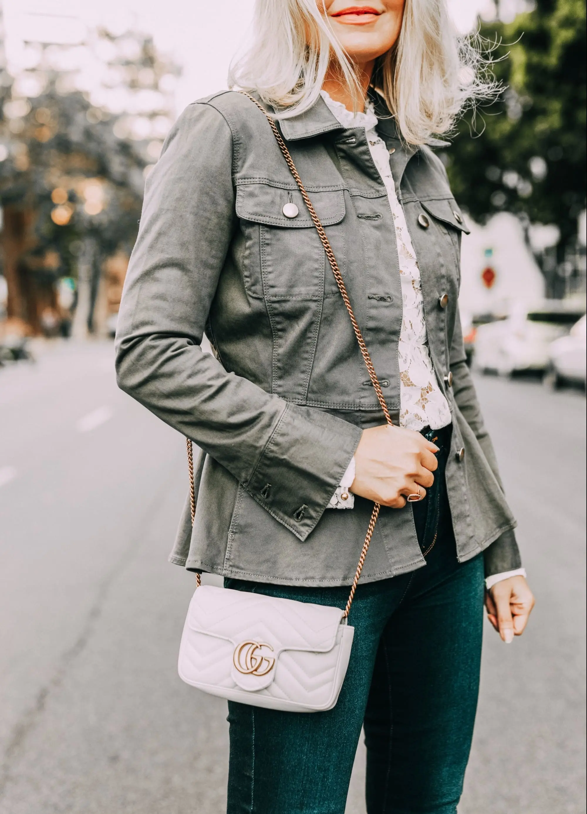 White Top Under $100, Fashion blogger Erin Busbee of BusbeeStyle.com wearing a white lace top by WAYF with dark wash skinny jeans by L'AGENCE, neutral Vince Camuto peep-toe mules, a white mini Gucci bag, and green peplum Frame jacket in San Diego, California