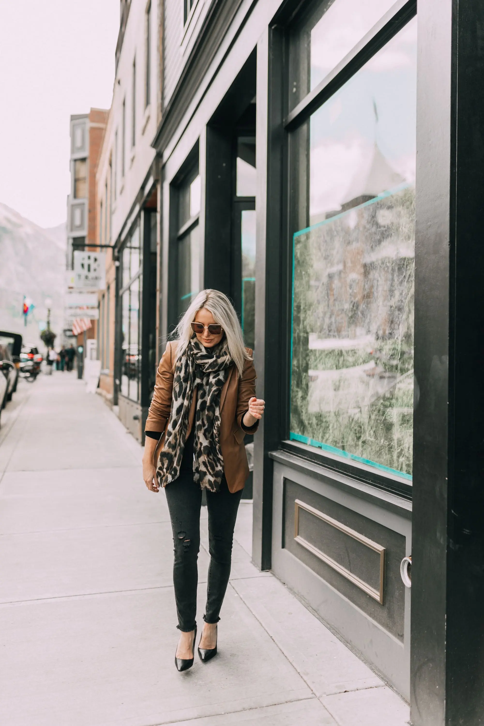 Brown and black outfit, fashion blogger Erin Busbee of BusbeeStyle.com wearing a brown leather blazer by Kobi Halperin, black distressed jeans by J Brand, black puff sleeve cashmere sweater by AQUA, gold Baublebar layered necklace, leopard print scarf, and black Jimmy Choo pumps in Telluride, Colorado