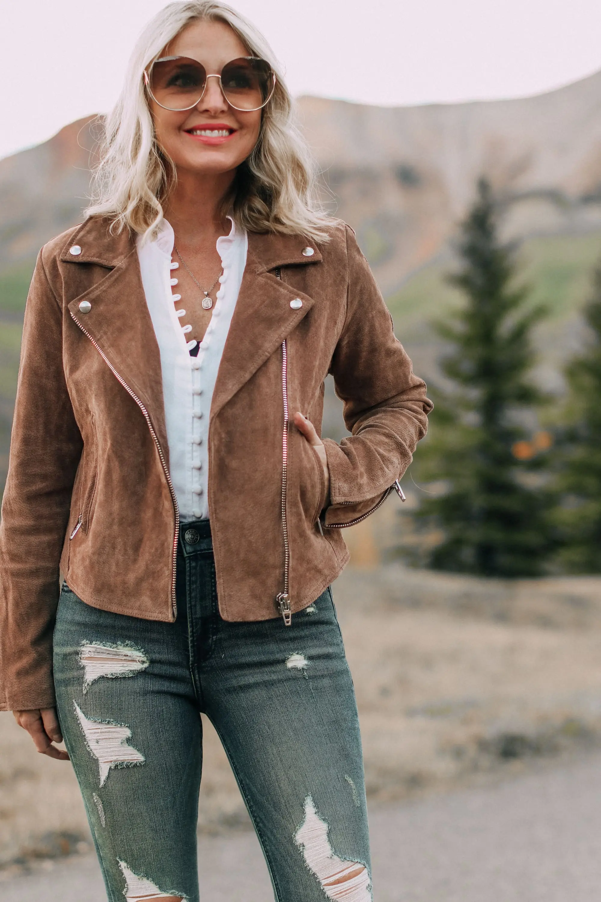 Blank NYC next level moto jacket on fashion blogger Erin Busbee of Busbee Style paired with Express white blouse and distressed jeans with beige Vince Camuto booties and Chloe sunglasses in Telluride, Colorado