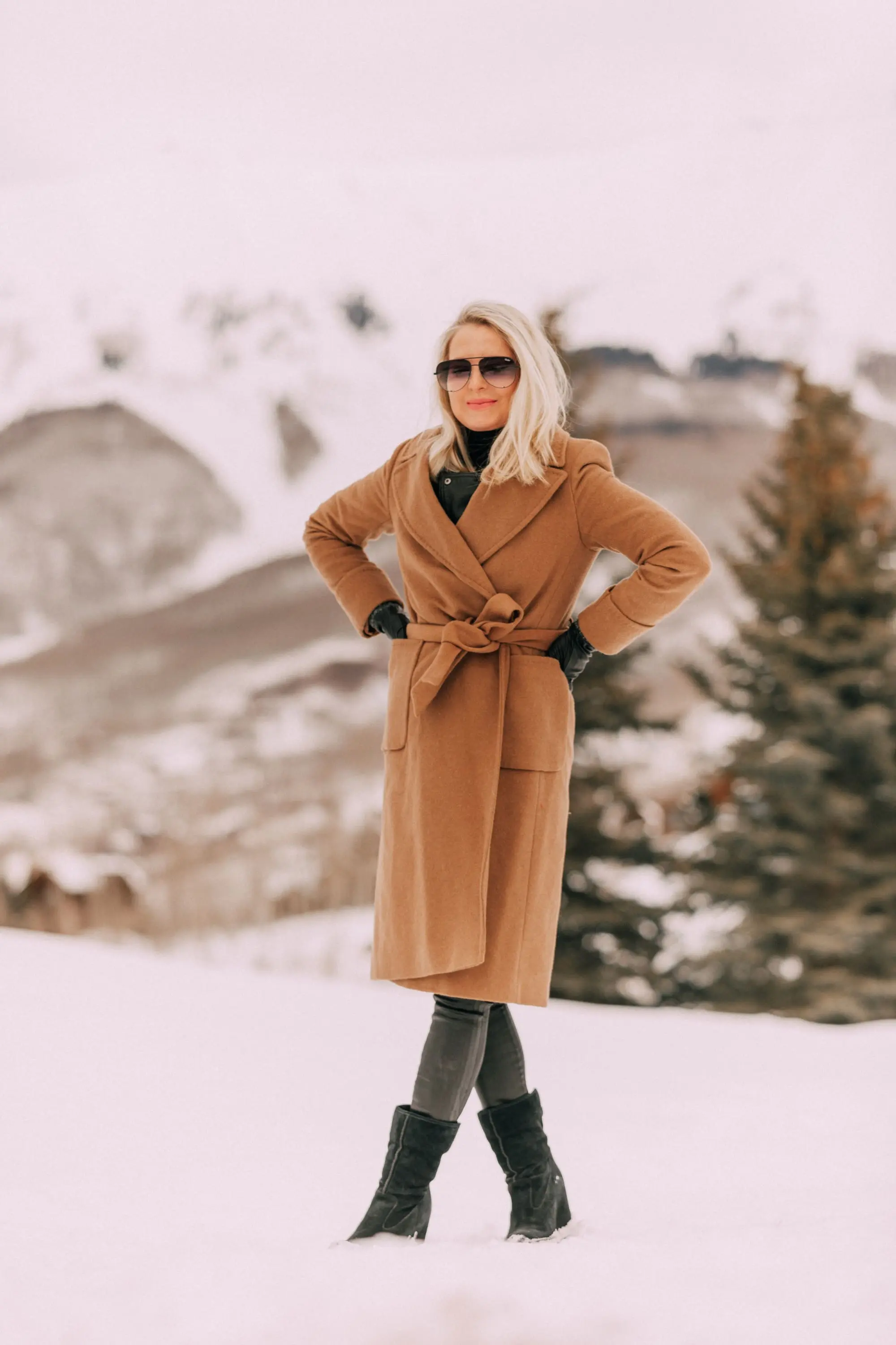 How To Layer A Moto Jacket, Fashion blogger Erin Busbee of BusbeeStyle.com wearing a black leather IRO moto jacket, Carolina Amato gloves, rocket leatherette skinny jeans by Citizens of Humanity, black cashmere turtleneck, Ugg wedge boots, and a wool camel coat by Mackage in Telluride, CO